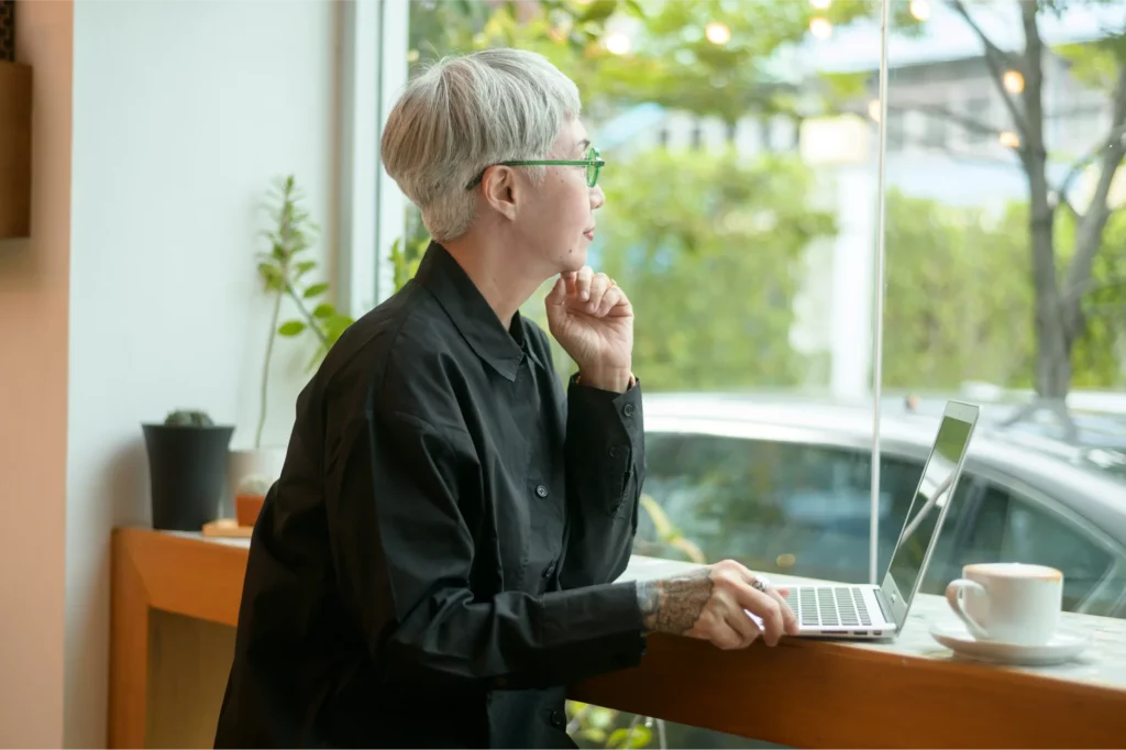 Mujer en una cafetería trabajando con un ordenador portátil y mirando por la ventana